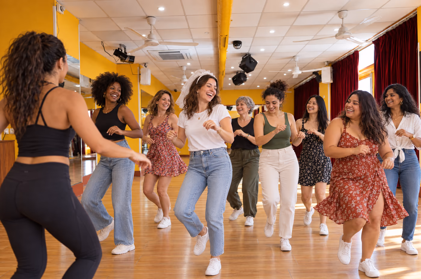 Un enterrement de vie de jeune fille dans la salle jaune : neuf amies de tous âges apprennent un pas de salsa en riant, la future mariée au centre.